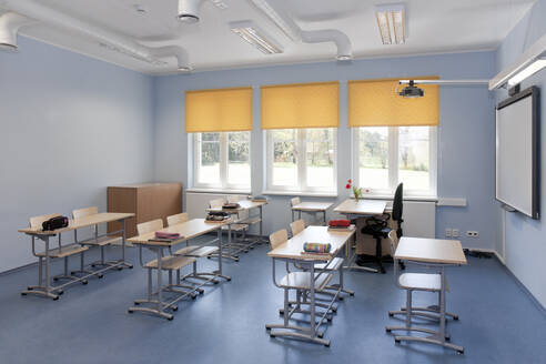 A school classroom with desks and chairs and yellow window blinds. - MINF16648