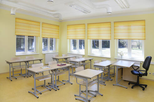 A school classroom with desks and chairs and yellow window blinds. - MINF16649