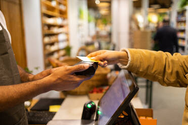 Unrecognizable customer paying with contactless credit card on terminal for purchase in modern shop - ADSF45683