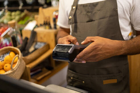 Unrecognizable male salesman wearing an apron standing by the counter while working in a shop in blurred background - ADSF45706