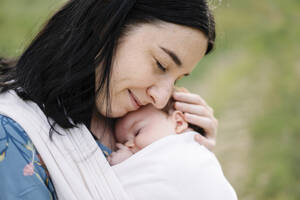 Lächelnde Mutter, die ihre Tochter im Tragetuch umarmt - SSYF00165