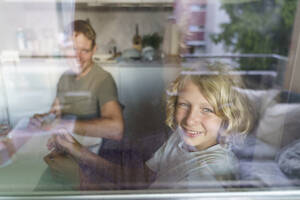 Lächelnder Vater und Sohn schauen von der Küche aus durchs Fenster - NJAF00443