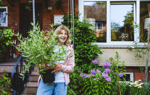 Smiling mature woman standing with sage plant - IHF01551