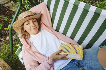 Lächelnde Frau mit Buch entspannt auf grüner Schaukel - IHF01558