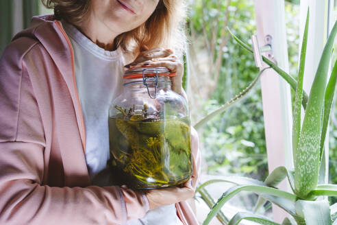 Reife Frau hält Glas mit fermentierten Gurken zu Hause - IHF01562