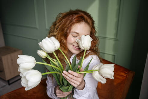 Young woman smelling bunch of tulip flowers at home - YBF00003