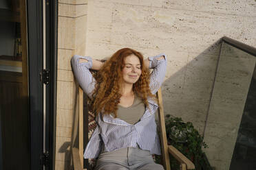 Smiling woman resting on chair in balcony - YBF00012