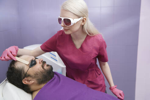 Dermatologe bei der Haarentfernungsbehandlung eines Kunden in der Klinik - AZF00548