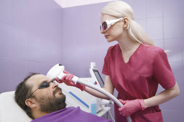 Arzt bei der Laser-Haarentfernungsbehandlung eines Kunden in einer Klinik - AZF00549