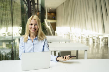 Smiling businesswoman working on laptop in office - SVKF01512