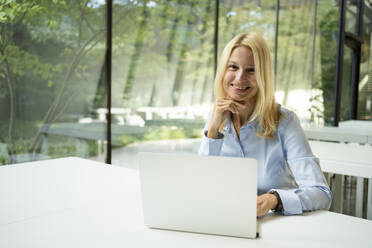 Lächelnde Geschäftsfrau vor einem Laptop sitzend - SVKF01514