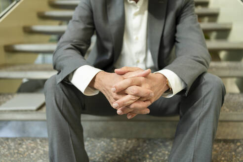 Businessman with hands clasped sitting on stairs - SVKF01515