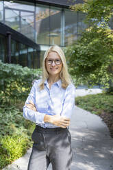 Confident businesswoman with arms crossed standing outside office - SVKF01518