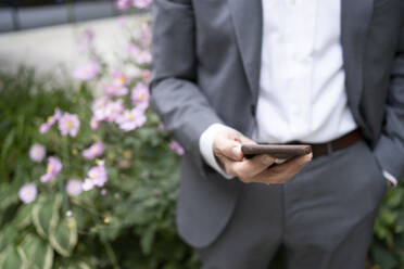 Businessman holding smart phone at office park - SVKF01526