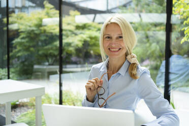 Lächelnde blonde Geschäftsfrau mit Brille im Büro - SVKF01530