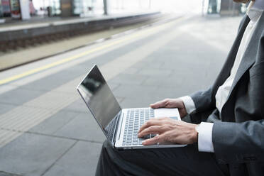 Businessman typing on laptop at railroad station - SVKF01542