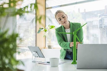 Young businesswoman examining wind turbine model at desk - UUF29584