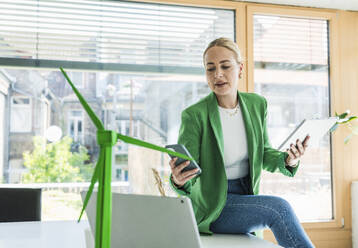 Businesswoman holding tablet PC and using smart phone in office - UUF29588