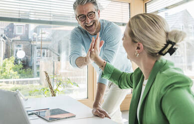 Cheerful businessman giving high-five to businesswoman in office - UUF29599