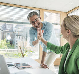 Ein glücklicher Geschäftsmann gibt einer Geschäftsfrau im Büro ein High-Five - UUF29600