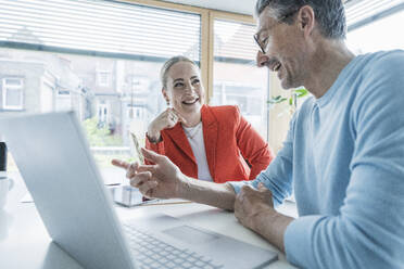 Happy businessman discussing with colleague at desk - UUF29603