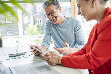 Happy mature businessman discussing strategy with businesswoman over tablet PC - UUF29610