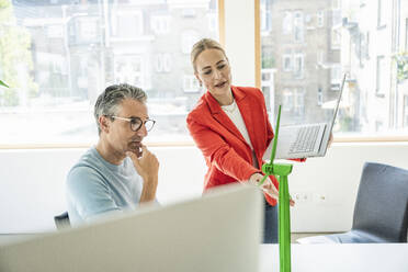 Smiling businesswoman having discussion on wind turbine model with colleague - UUF29613