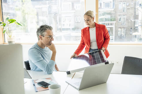 Young businesswoman discussing over solar panel with colleague in office - UUF29616