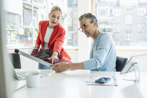 Young businesswoman discussing over solar panel with colleague at desk - UUF29617