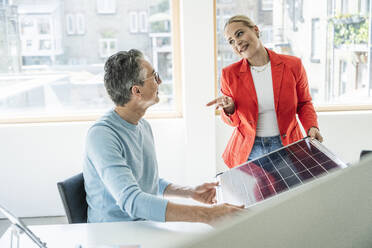 Young businesswoman gesturing and discussing over solar panel with colleague in office - UUF29618