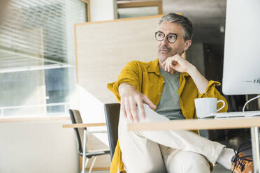 Thoughtful businessman sitting with coffee cup at desk - UUF29629