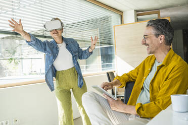 Happy mature businessman with colleague wearing virtual reality simulators - UUF29637