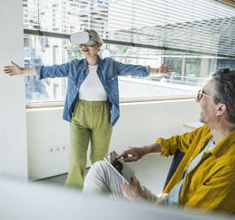 Happy mature businessman with colleague wearing virtual reality simulators in office - UUF29638