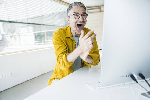 Gut gelaunter Geschäftsmann bei der Arbeit an einem Desktop-PC im Büro - UUF29642