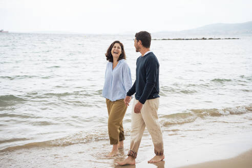 Cheerful couple holding hands and walking at beach - JOSEF19991