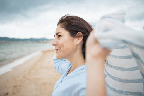 Smiling woman holding scarf at beach - JOSEF19992