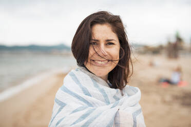Lächelnde Frau in Schal eingewickelt am Strand - JOSEF20005