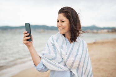 Eine glückliche Frau hält einen Moment am Strand mit ihrem Smartphone fest und lächelt für ein Selfie - JOSEF20007