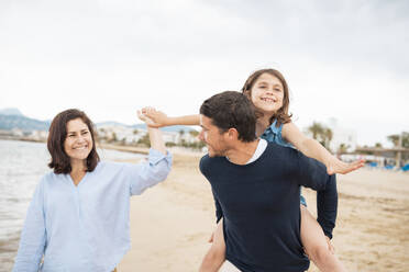 Smiling woman with father giving piggyback ride to daughter at beach - JOSEF20018