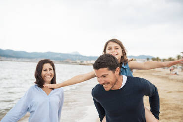 Happy mother with father giving piggyback ride to daughter at beach - JOSEF20020