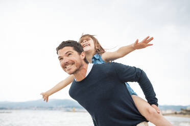 Cheerful father giving piggyback ride to daughter at beach - JOSEF20022