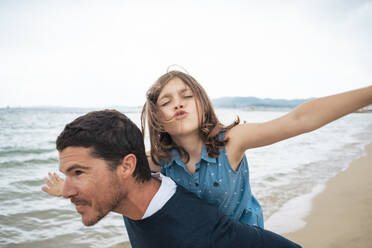 Smiling father giving piggyback ride to daughter at beach - JOSEF20023