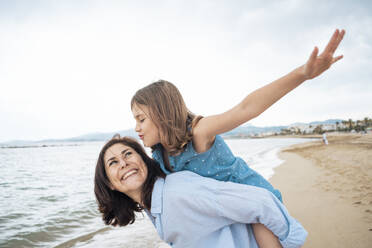 Cheerful mother giving piggyback ride to daughter at beach - JOSEF20026