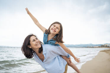 Happy woman giving piggyback ride to daughter at beach - JOSEF20028