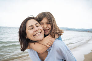 Glückliches Mädchen umarmt Mutter am Strand unter Himmel - JOSEF20031