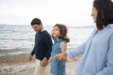 Happy father and mother holding hands with daughter at beach - JOSEF20038