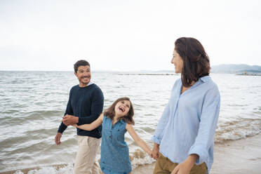 Fröhliches Mädchen, das mit Vater und Mutter am Strand spazieren geht - JOSEF20040