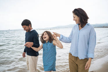 Vater und Mutter halten sich mit ihrer Tochter an den Händen und genießen den Urlaub am Strand - JOSEF20041