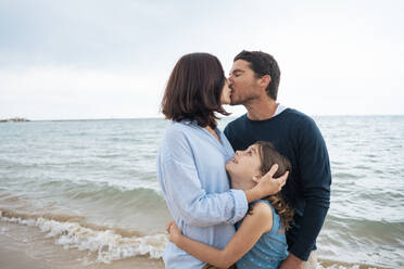 Glückliches Mädchen mit Vater und Mutter, die sich am Strand küssen - JOSEF20051