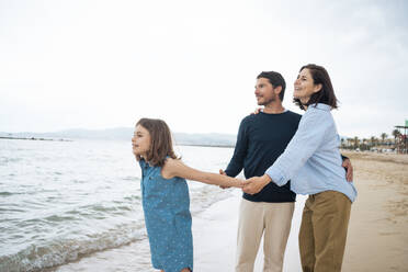 Happy mother and father holding hands with daughter at beach - JOSEF20053